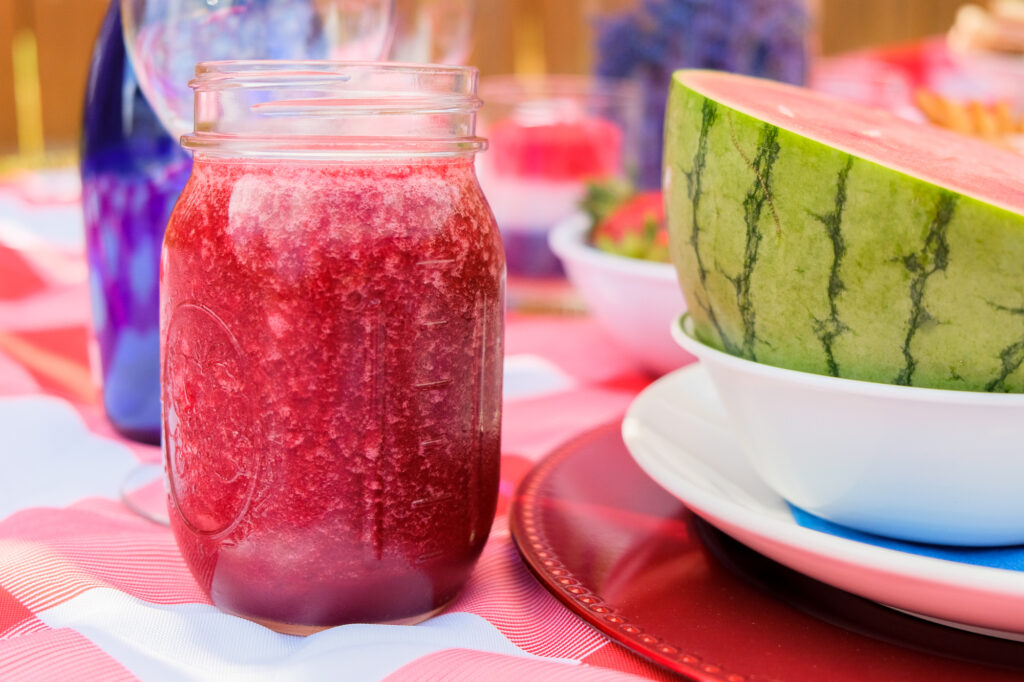 red smoothie in a mason jar, sitting next to cut watermelon