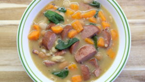 sausage and bean soup in a white bowl with a wood background