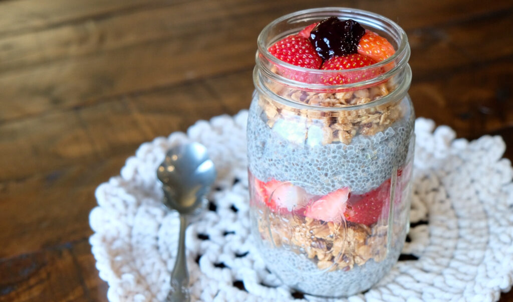 chia pudding layered in a mason jar with fresh strawberries, granola and blackberry preserves