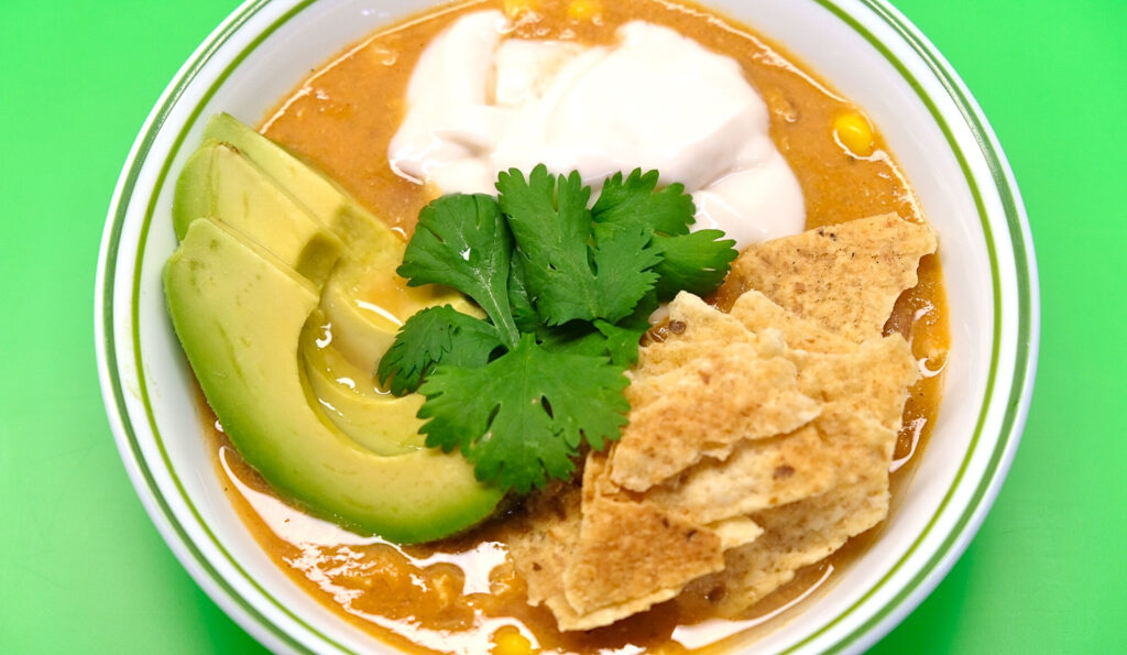 chicken tortilla soup with toppings on a green background