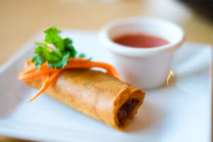 egg roll with dip and a garnish on a white plate