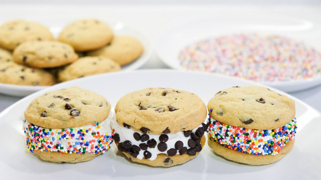 three cookie ice cream sandwiches with sprinkles and chocolate chips on a white plate