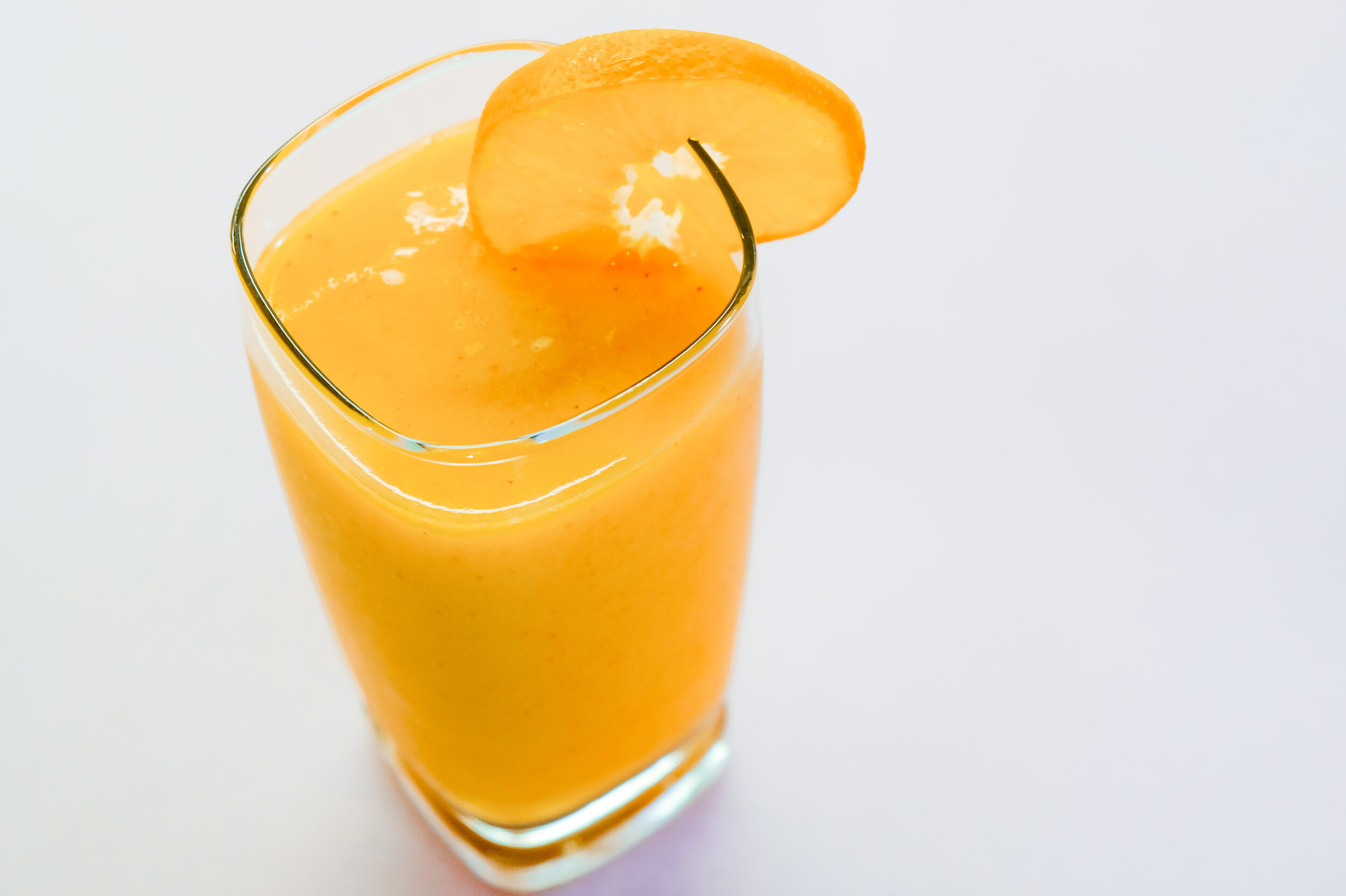 mango carrot citrus smoothie in a clear glass with orange slice