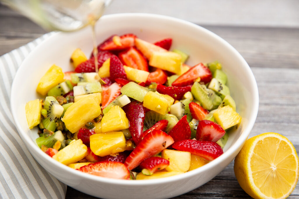 pouring honey lemon dressing over a bowl of tropical fruit