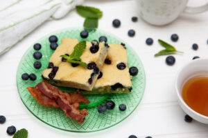 blueberry sheet pan pancakes on a green plate, white background coffee and syrup in a bowl