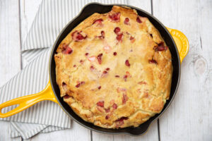 strawberry clafoutis in a yellow skillet with a white wood background