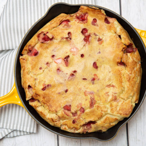 strawberry clafoutis in a yellow skillet with a white wood background