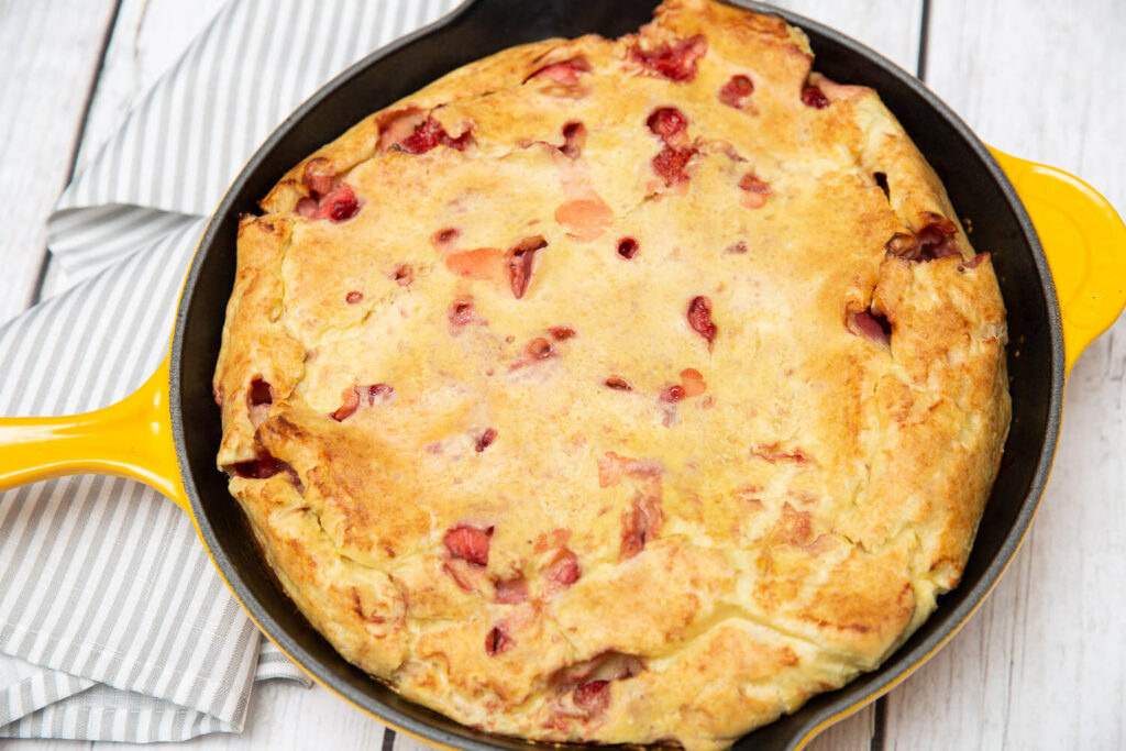 strawberry clafoutis in a yellow skillet with a white wood background