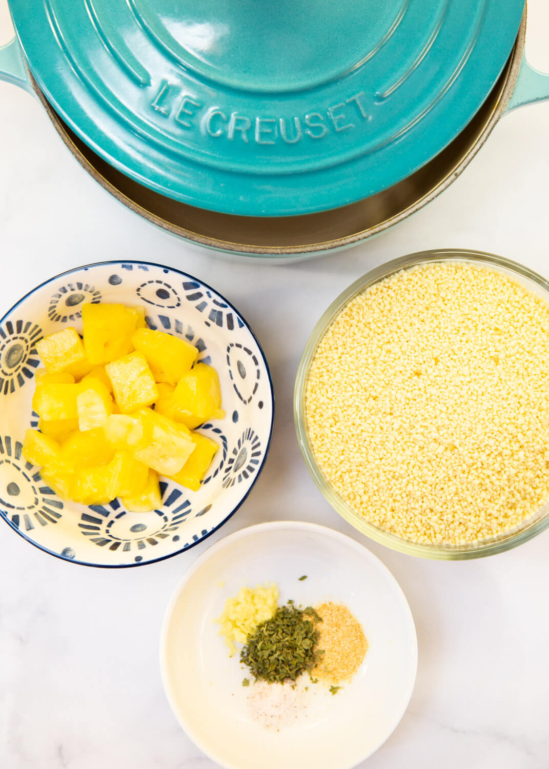 turquoise dutch oven, bowl of pineapple chunks, dry couscous and some spices